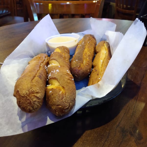 Four pretzel sticks with salt and a side of cheese dip on a wooden table.