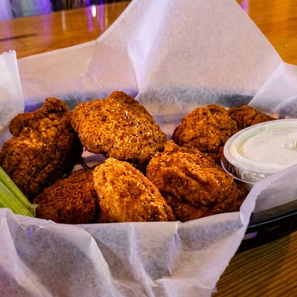 Crispy fried chicken wings with celery sticks and ranch dressing in a basket on a wooden table.