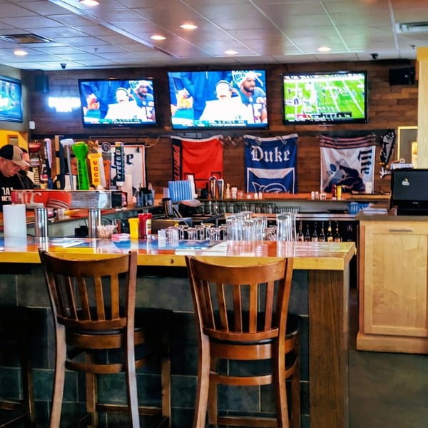 A sports bar with a bartender, multiple TVs showing sports, and bar stools along a counter.