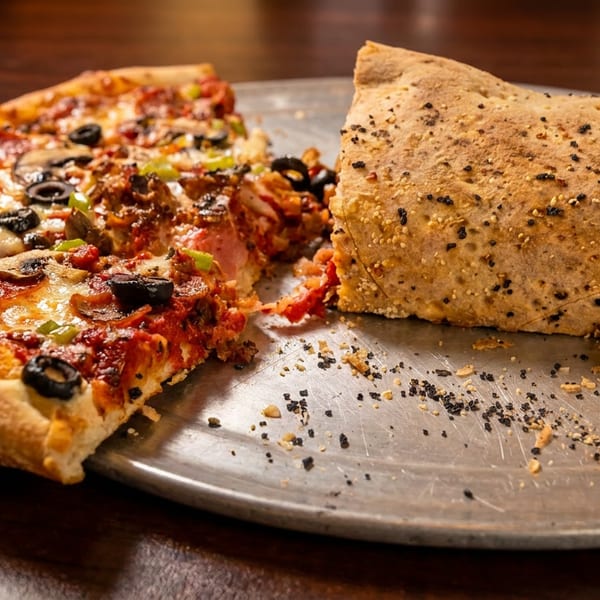 Half-eaten pizza with pepperoni, olives, and mushrooms next to a calzone on a metal tray.