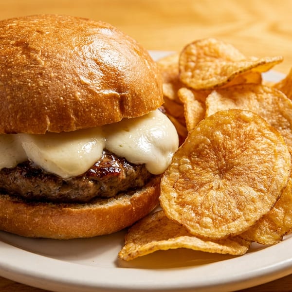 Cheeseburger with melted white cheese and a side of crispy potato chips on a white plate.