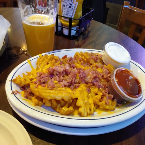 Loaded waffle fries with melted cheese and bacon bits, served with dipping sauces and a beer.